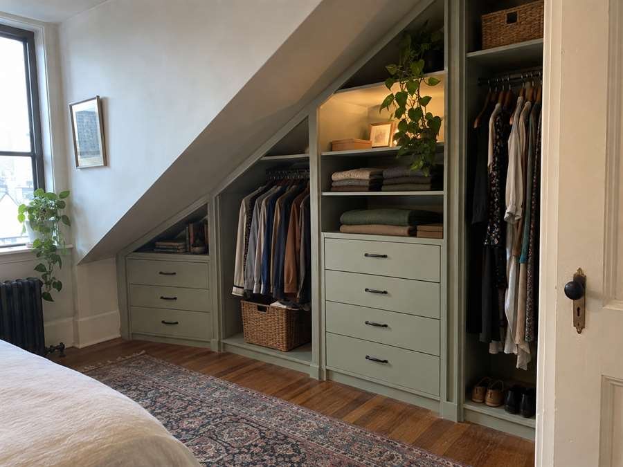 Built-in closet fitted under a sloped ceiling with sage drawers, shelves and hanging space