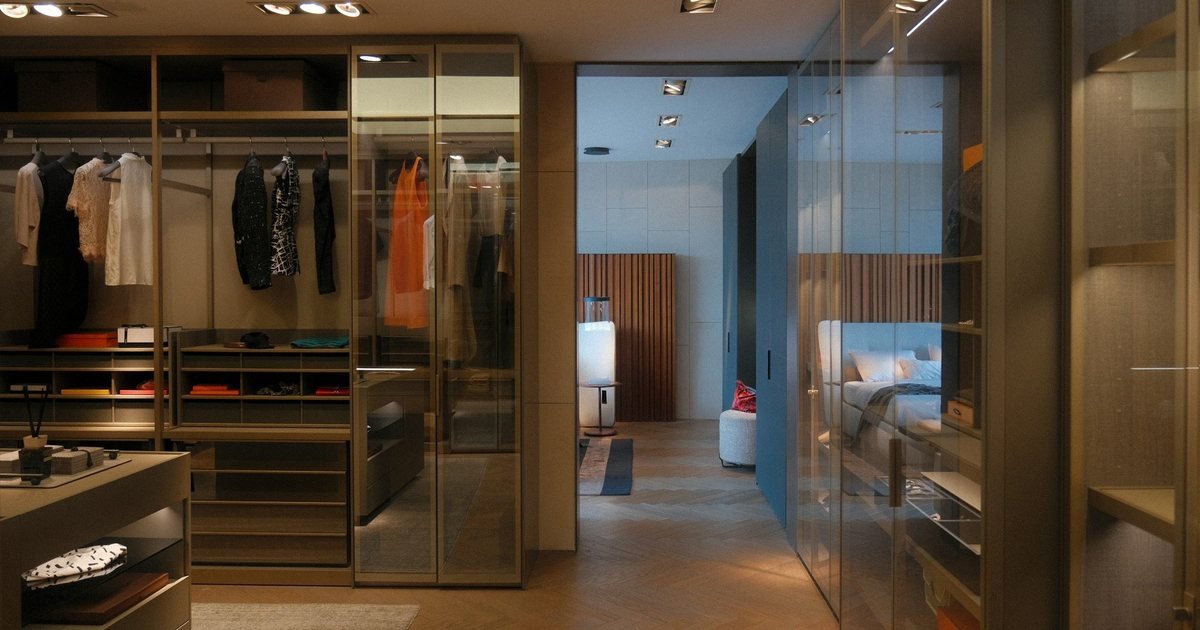 Dressing room with bronze-framed glass wardrobe doors, open hanging rails and a center island, opening onto a bedroom